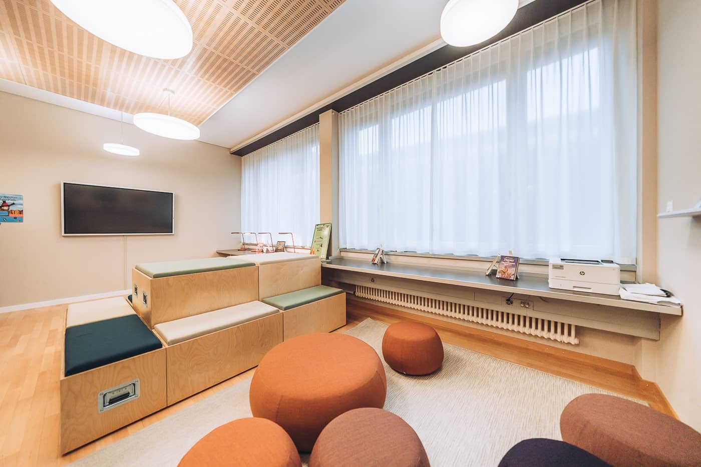 Vor einer Fensterfront ist eine gem&uuml;tliche Sitzecke mit Teppich und Hockern eingerichtet